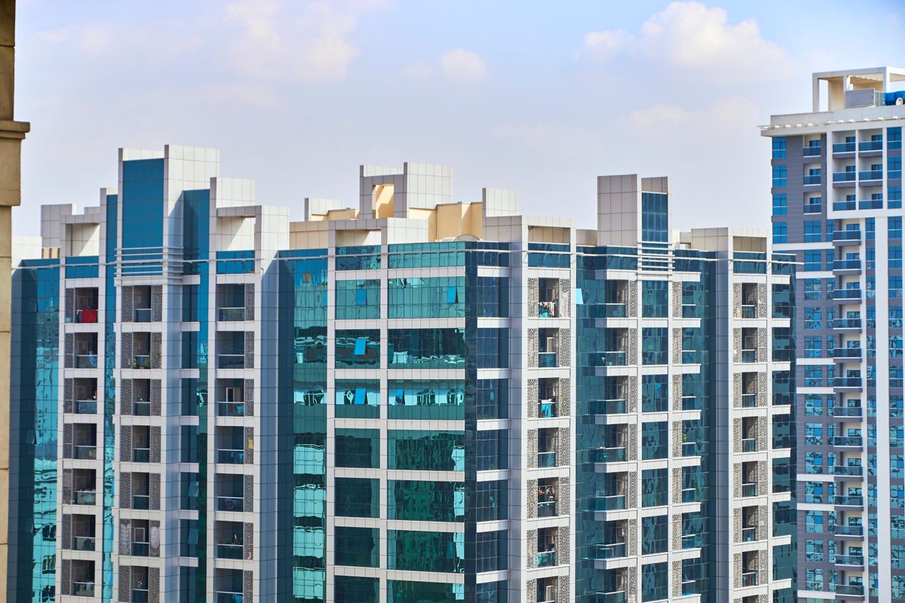 about-01 A cityscape view of modern high-rise buildings with reflective glass facades under a blue sky.