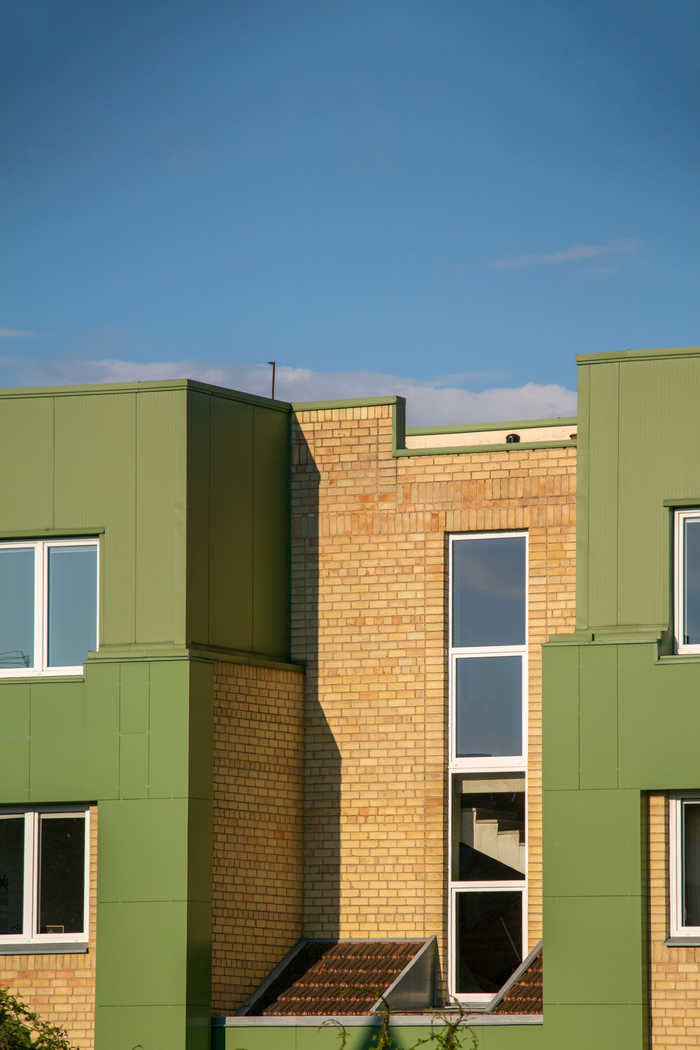 testimonials-img Sunlit modern building exterior with green and brick facade under clear blue sky.