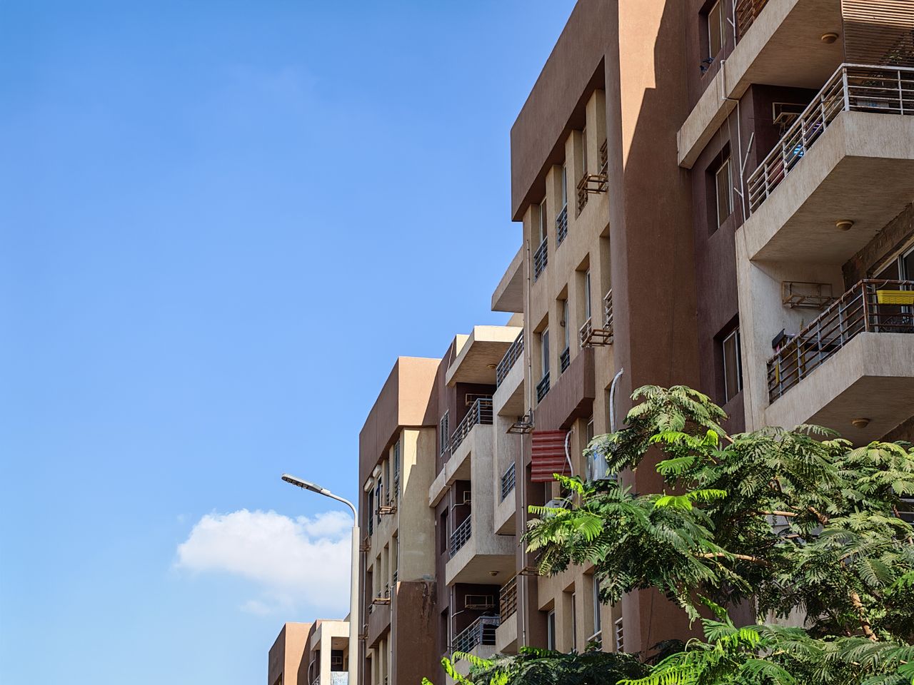 story-img Urban apartment building against a bright blue sky with foliage in the foreground.
