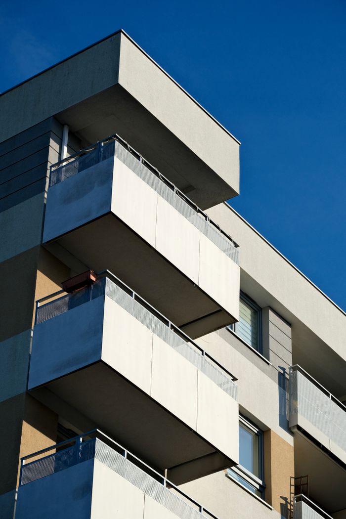 services-02 Close-up of a modern apartment building showcasing minimalist design against a clear blue sky.